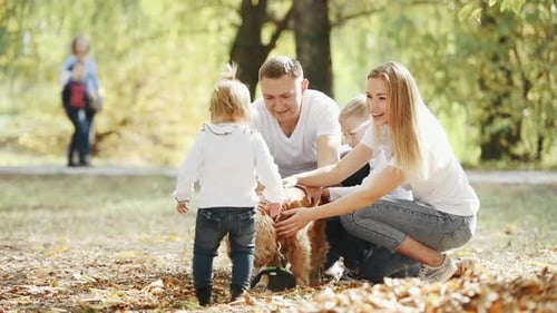 Cheerful young family have a rest in autumn park together and petting dog