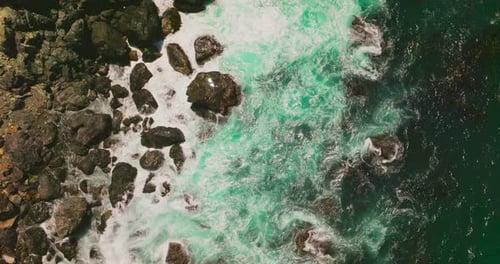 Lots of stones washed by the white foamy waves of the ocean.