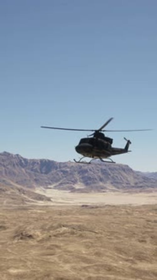 A Helicopter Flying Over a Desert with Mountains in the Background