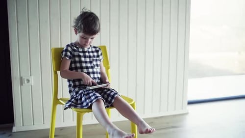 Child Sits in Chair Using Mobile Tablet Indoors