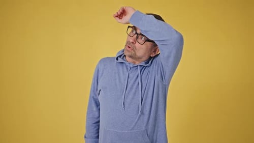 Man Overheated and Fanning Himself on Yellow Backdrop
