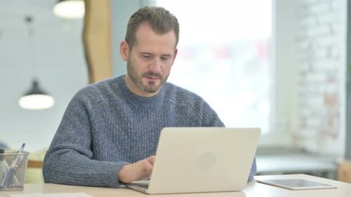 Man Smiles While Working on Laptop Computer Indoors