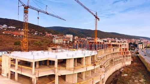 Drone flight along the building under construction. Two yellow crane tower over the building.