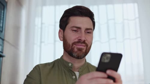 Bearded Man Smiling Using Smartphone Indoors