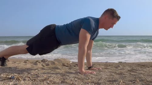 A young Caucasian man with short hair doing push-ups (sports) on the sand beach by the sea with his