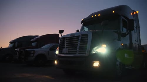 Parked Semi Trucks in Evening With Headlights On