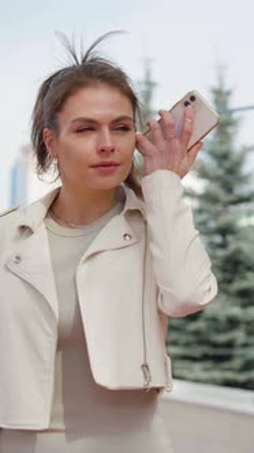 Young Serious Brunette Listens to a Voice Message on Her Smartphone on the Street