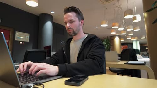 Focused Young Man Working at Laptop Computer at Office Workplace