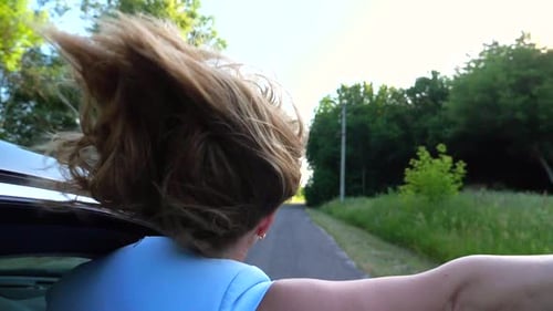 Woman Leaning Out of Car Window and Holding Her Hand Out While Riding on Countryside Road Girl
