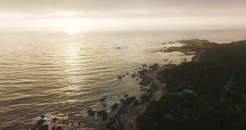 Ragged rough rocky shore covered with greenery. Beautiful Pacific Ocean in the rays of setting sun.