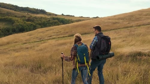 Couple Hiking Across Grassy Hills With Backpacks