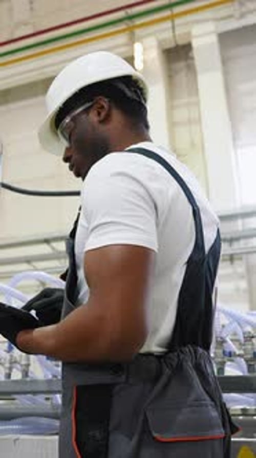 African American Worker in Uniform Checks the Cooling System at the Factory Vertical Video