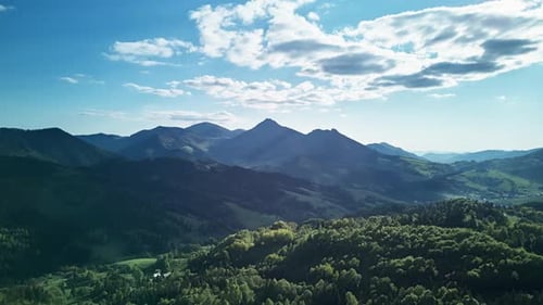 Hyperlapse aus der Luft über grünen Bergen und Wäldern an einem sonnigen Frühlingstag