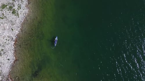 A person paddle boarding on a blue board. Wide rotating aerial view.