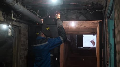 Back Shot of Professional Welder in Safety Suit and Protective Mask Welds Metal Door Using Welding