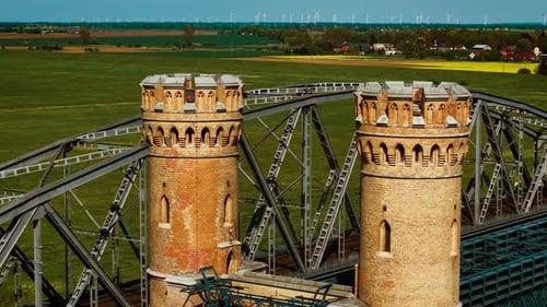 Puente ferroviario de acero que atraviesa torres gemelas de ladrillo sobre un cruce de celosía metálica de Green Fields
