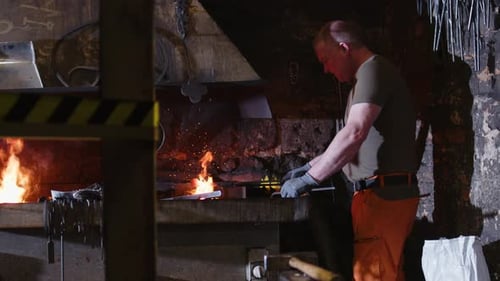 Man Forging Hot Metal in Dark Workshop