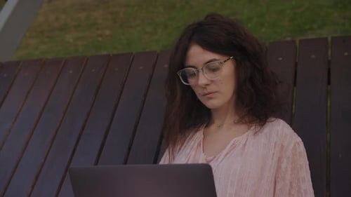 Handheld Close Up of a Curly Caucasian Woman Working on Her Laptop Computer on a Park Bench