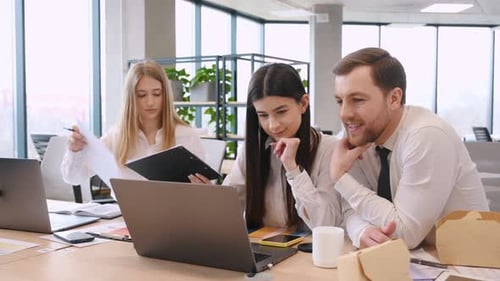 Sitting by the laptop, talking. Group of people working in the modern office together