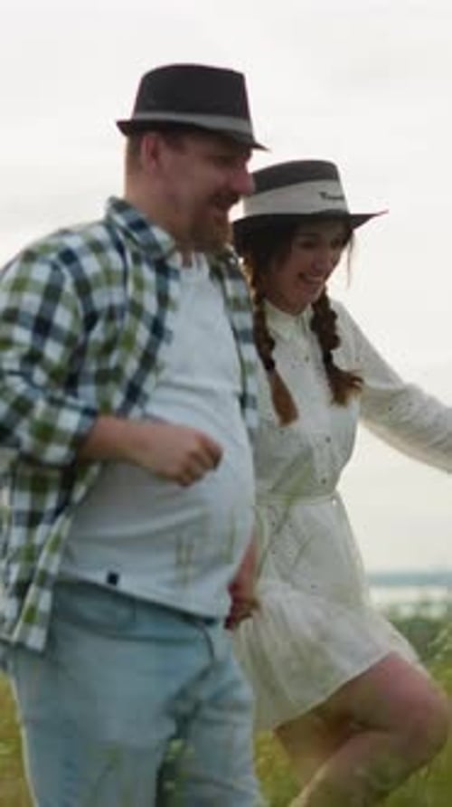 Joyful Couple Holding Hands and Running Through a Grassy Field at Sunset