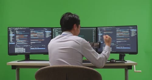 Happy Developer Looking At Code On Mobile Phone While Work With Multiple Screens In Green Screen
