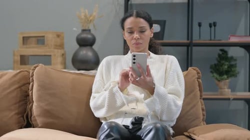 Femme africaine naviguant sur Internet au téléphone à la maison