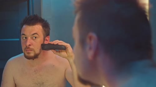 Man Shaves Beard with Electric Razor in Bathroom