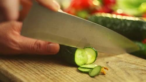 A Man's Hand Cuts a Green Cucumber with a Large Knife