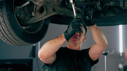 Close Up an Auto Mechanic at Service Station Checks a Car Being Lifted on a Lift Fixing Problems