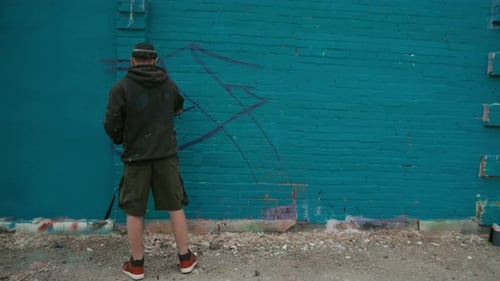 Jovem desenhando etiqueta de grafite na parede azul ao ar livre