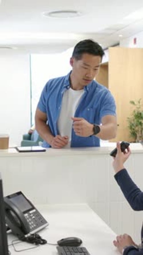 Vídeo vertical: recepcionista estendendo o leitor na recepção, homem de camisa azul tocando no relógio para pagar
