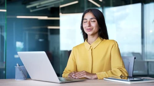 Calm young businesswoman sitting at desk in modern office with closed eyes practicing breathing