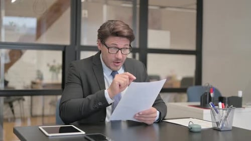 Middle Aged Businessman Cheering while Reading Documents in Office