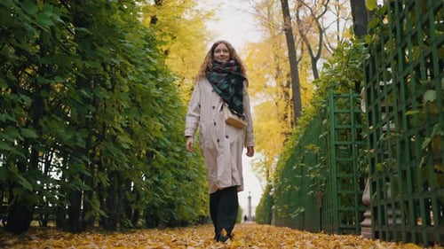 Pensive Woman in a Raincoat Walks in an Autumn Park Strewn with Yellow Leaves