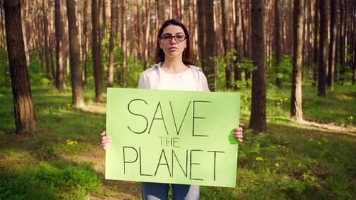 Young woman volunteer activist in forest protest with poster save the planet Female student