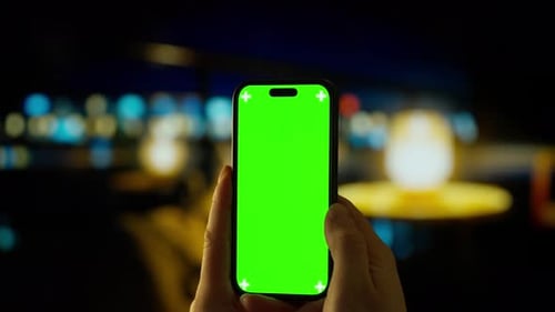 Person Holding Modern Smartphone with Bright Green Chroma Key Screen in Dimly Lit Indoor Environment