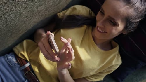 Top view of caucasian woman lying on sofa and browsing phone. Shot with RED helium camera in 8K.