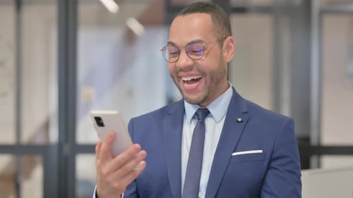 Man Celebrating Success While Using Smartphone in Office