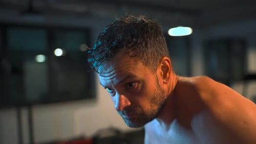 Alone Boxer is Working Out Blows on a Punching Bag in a Gym in Evening