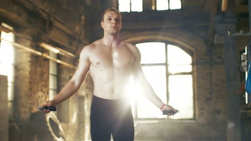 Muscular Shirtless Fit Man Exercises with Jump Skipping Rope in a Deserted Factory Hardcore Gym.