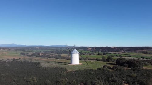orbit around traditional white windmill with mountains in the distance and green meadows typical med