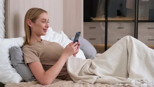 Woman Relaxing and Smiling Using Mobile Phone in Bed