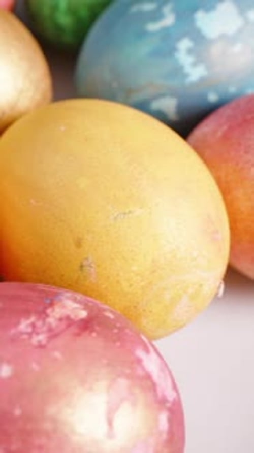 Vertical video. Close-up of a variety of vibrant Easter eggs, including golden, orange, pink, and