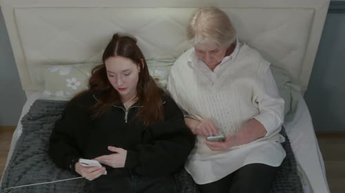 Woman and Senior Using Smartphones Lying on Bed