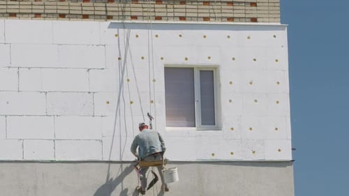 Construction Worker Applies Material to Building Exterior