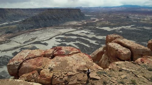 Drone Shot of Woman Walking to the Edge of Mesa Cliff Above Deep Dry Canyon in Desert of Utah USA