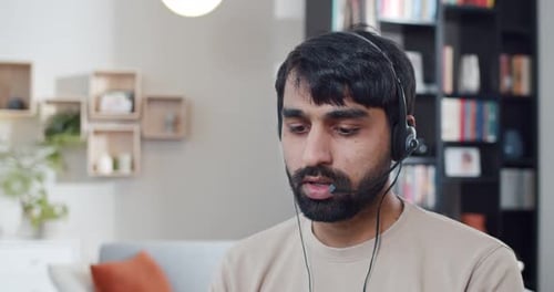 Close Up of Arabian Young Man in Headset Working at Computer and Talking While Videochatting at Home