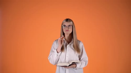 Thoughtful Young Blonde Woman Holding Pencil and Book, Colorful Studio Shot