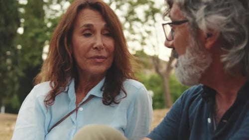 Close-up of beautiful elderly couple chatting while sitting on the grass in the park
