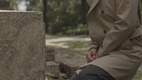 Man Sitting Down on Knees by Grave at Cemetery